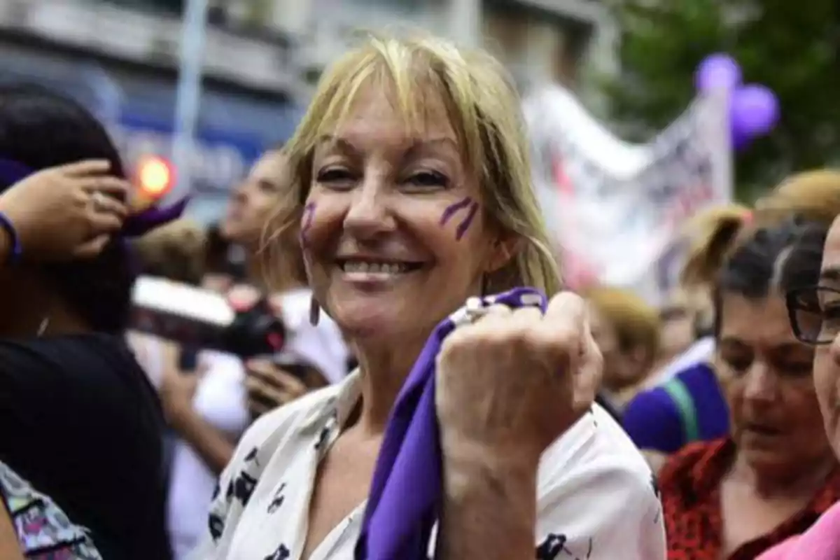 Smiling woman with purple paint on her cheeks and a purple scarf in her hand participating in a demonstration surrounded by other people Smiling woman with purple paint on her cheeks and a purple scarf in her hand participating in a demonstration surrounded by other people