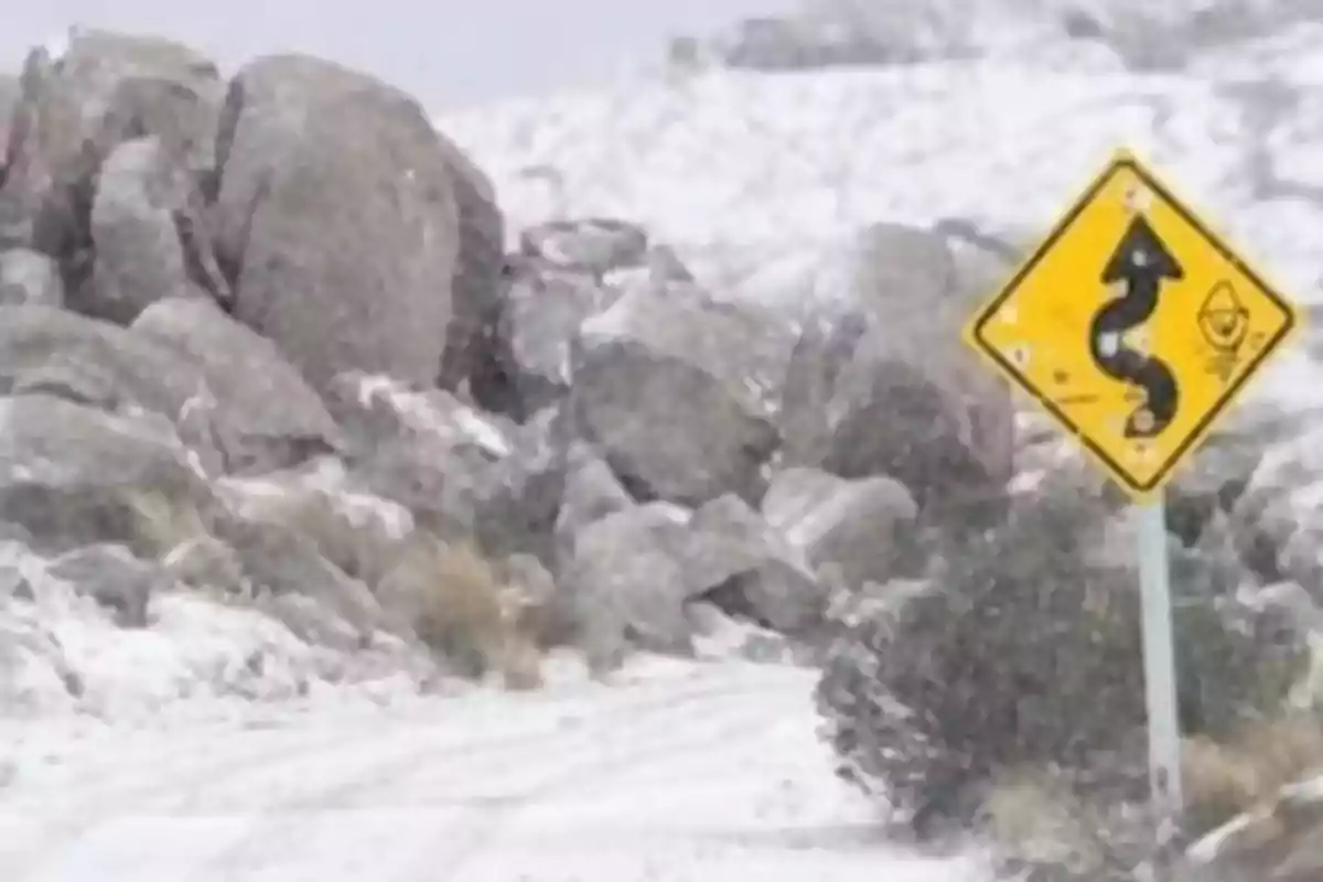 Snowy road with large rocks and a yellow traffic sign indicating dangerous curves Snowy road with large rocks and a yellow traffic sign indicating dangerous curves