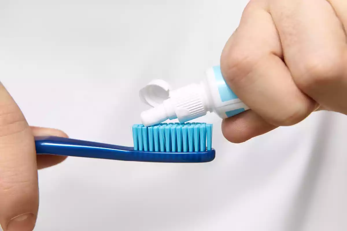 Mano colocando pasta dental sobre un cepillo de dientes azul