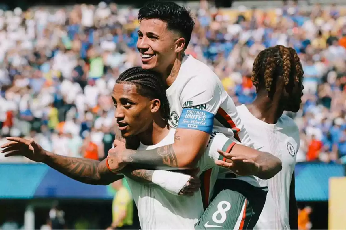 Jugadores de fútbol celebran un gol durante un partido con el estadio lleno de aficionados al fondo Jugadores de fútbol celebran un gol durante un partido con el estadio lleno de aficionados al fondo