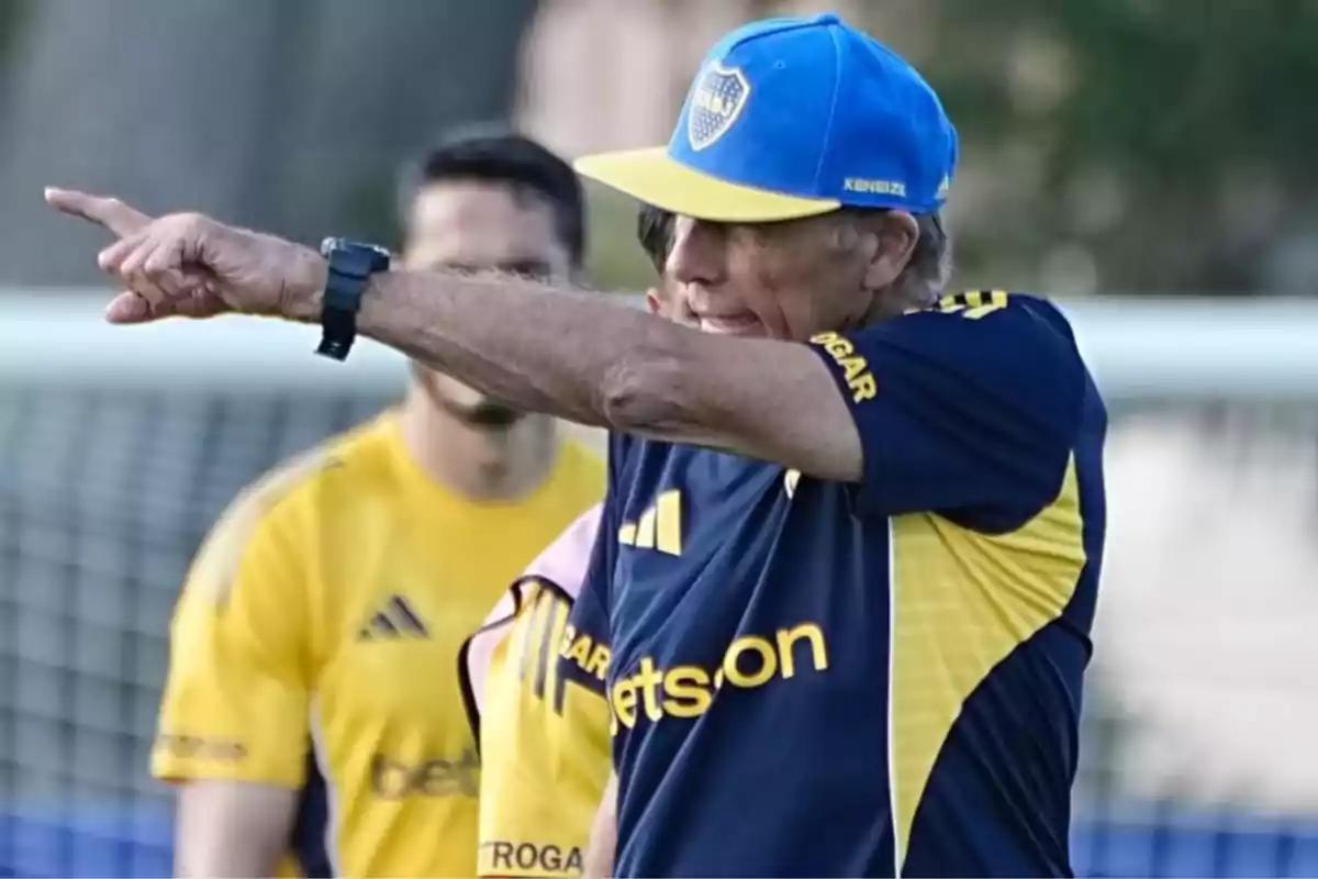 Soccer coach wearing a blue and yellow cap giving instructions on a training field