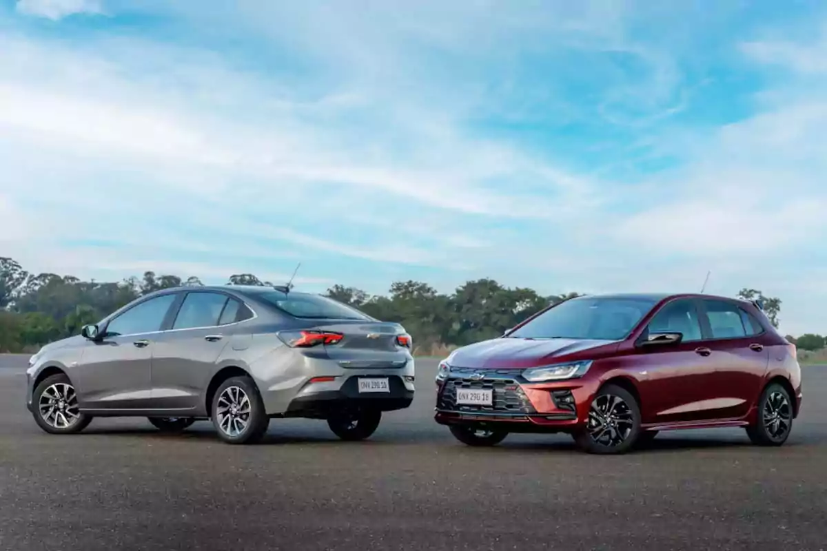 Dos autos Chevrolet estacionados sobre asfalto con cielo azul y árboles al fondo Dos autos Chevrolet estacionados sobre asfalto con cielo azul y árboles al fondo