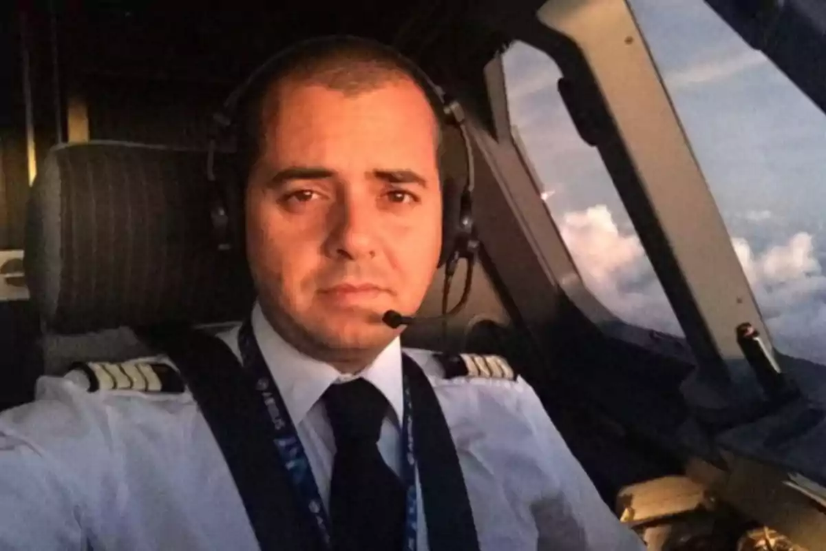 Piloto con uniforme y auriculares sentado en la cabina de un avión durante el vuelo con el cielo visible a través de la ventana