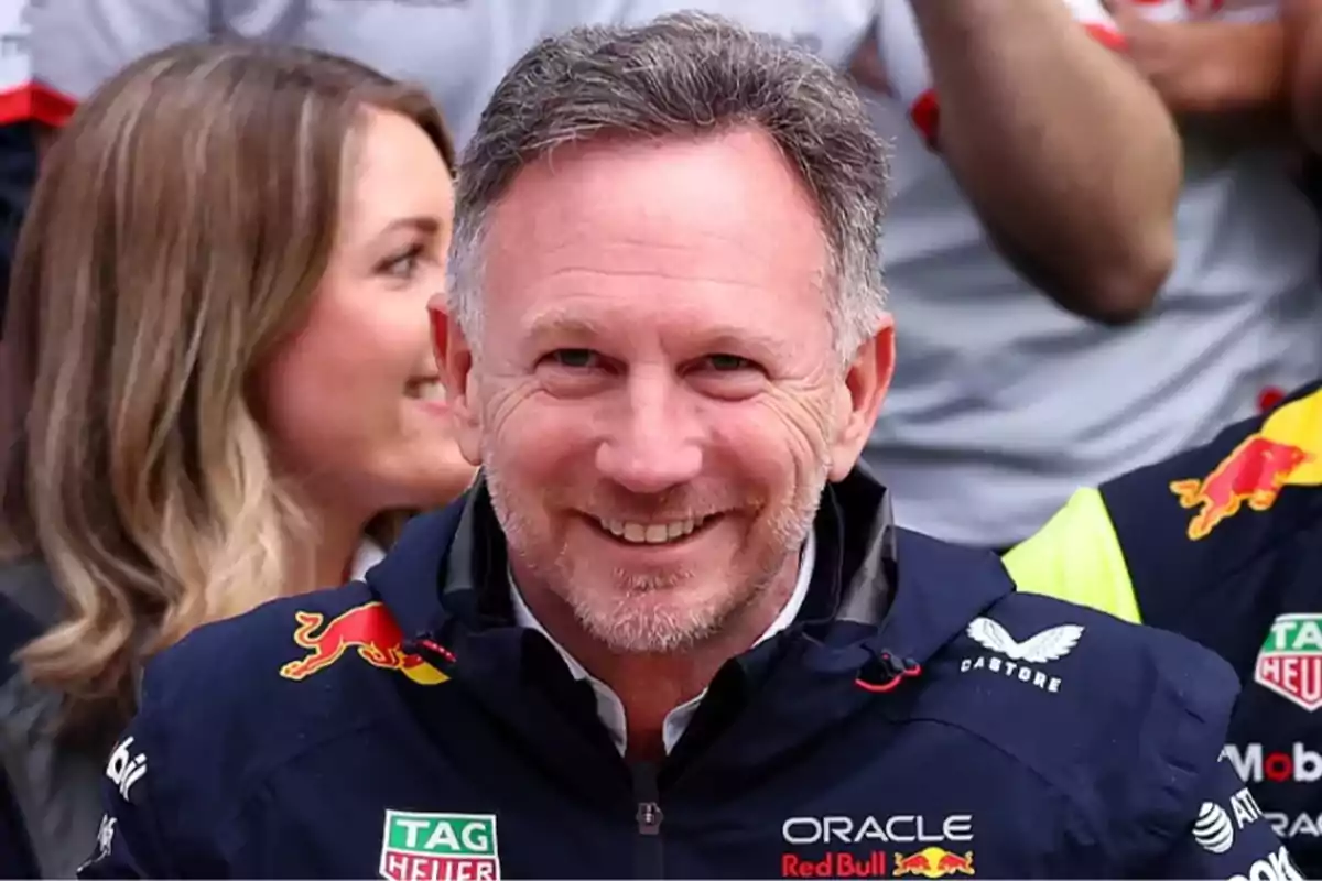 Hombre sonriente con chaqueta de Red Bull Racing en un evento deportivo rodeado de otras personas
