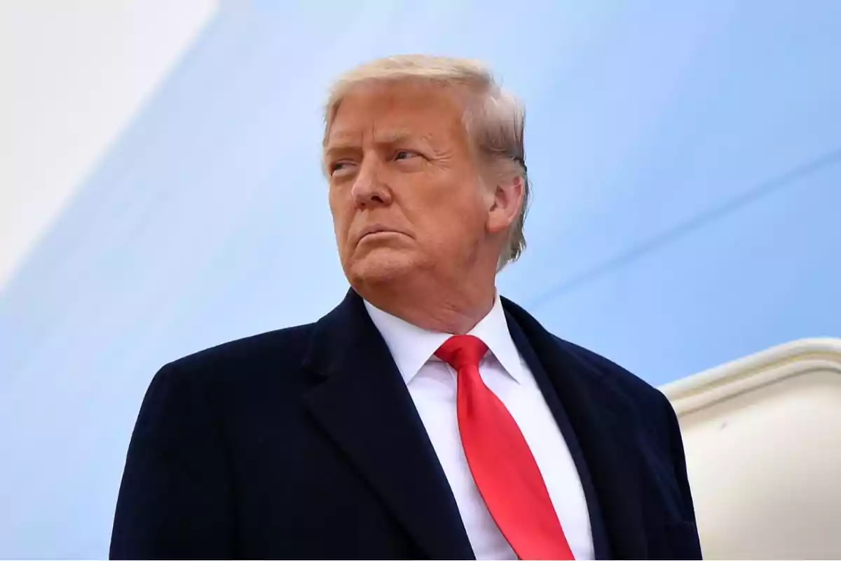 Blond-haired man in a dark suit and red tie looking to the side against a light blue background Blond-haired man in a dark suit and red tie looking to the side against a light blue background