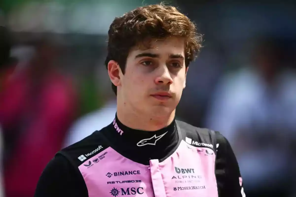 Joven piloto de automovilismo con uniforme negro y rosa de un equipo de carreras, fondo desenfocado con personas y colores brillantes