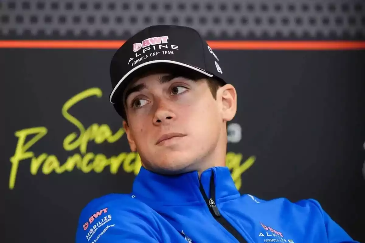 Piloto de automovilismo con gorra y chaqueta azul de un equipo de Fórmula 1 durante una conferencia de prensa Piloto de automovilismo con gorra y chaqueta azul de un equipo de Fórmula 1 durante una conferencia de prensa