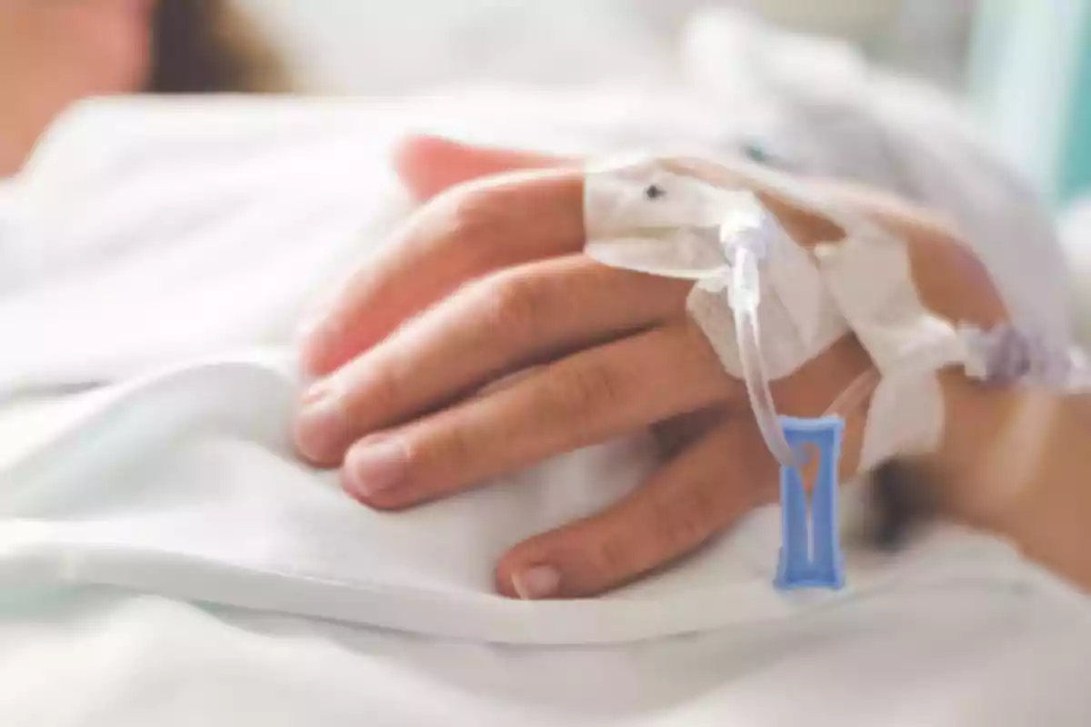 Hand of a person with an intravenous line resting on a white sheet in a hospital setting Hand of a person with an intravenous line resting on a white sheet in a hospital setting