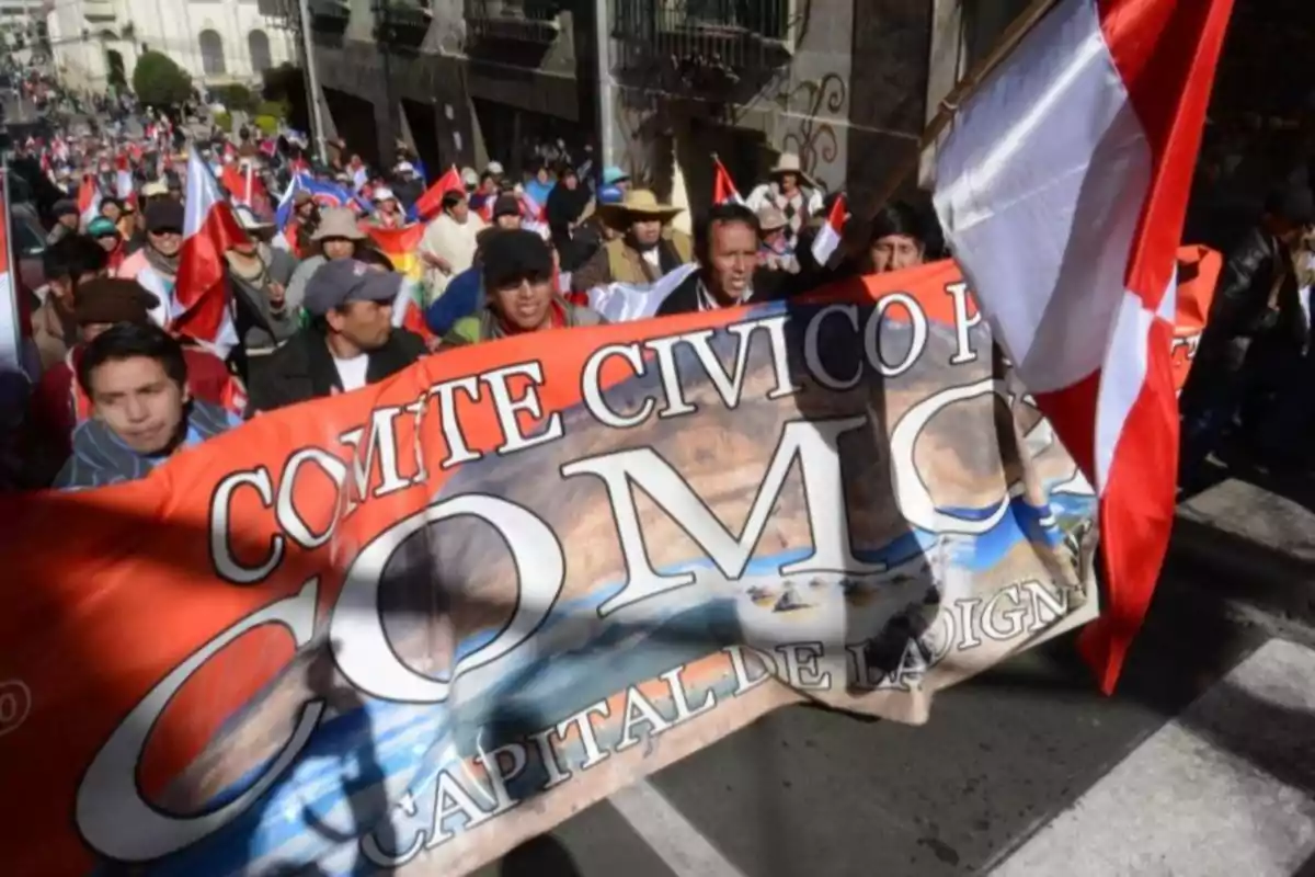 Demonstration of people marching down the street with a large banner from the Oruro Civic Committee and several red and white flags Demonstration of people marching down the street with a large banner from the Oruro Civic Committee and several red and white flags
