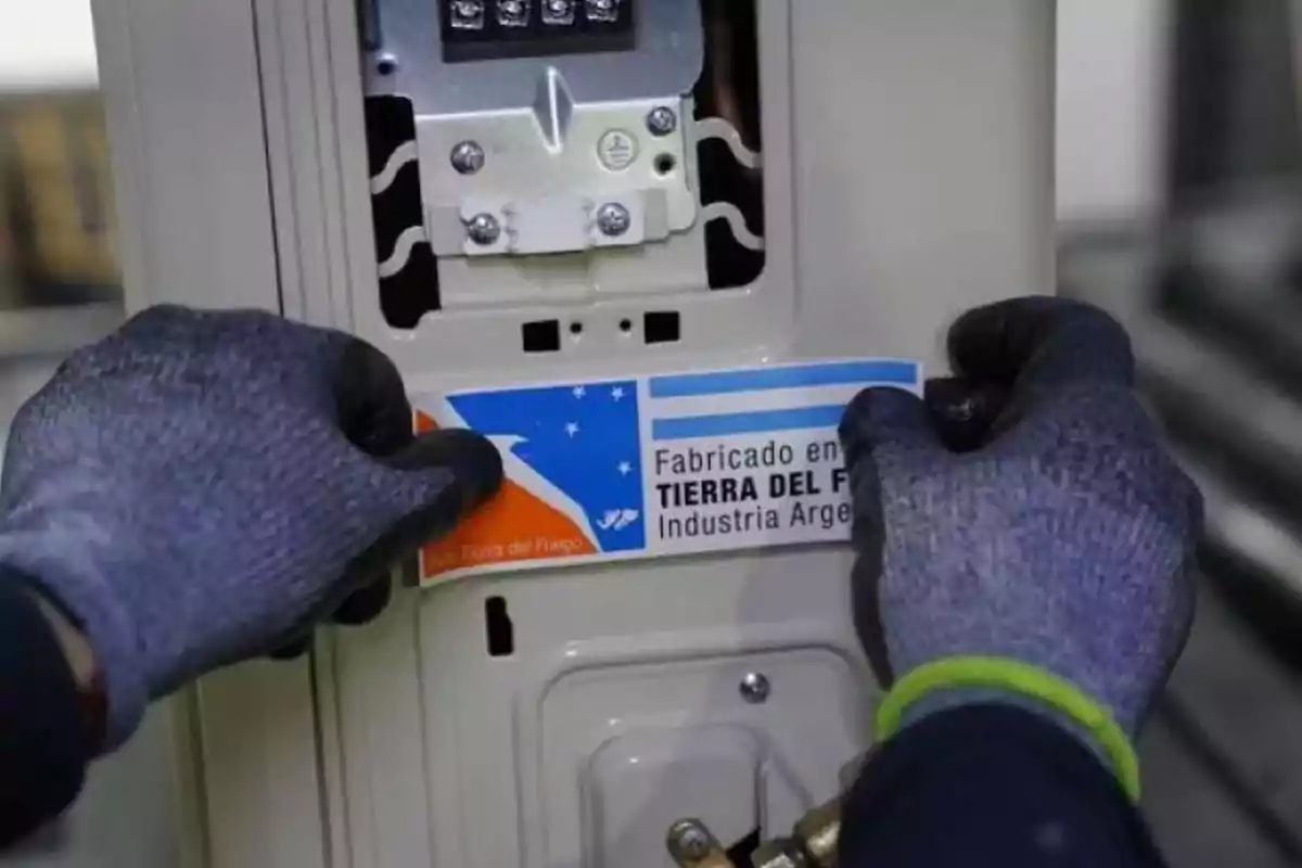 Manos con guantes colocando una etiqueta que dice Fabricado en Tierra del Fuego Industria Argentina en un electrodoméstico. Manos con guantes colocando una etiqueta que dice Fabricado en Tierra del Fuego Industria Argentina en un electrodoméstico.