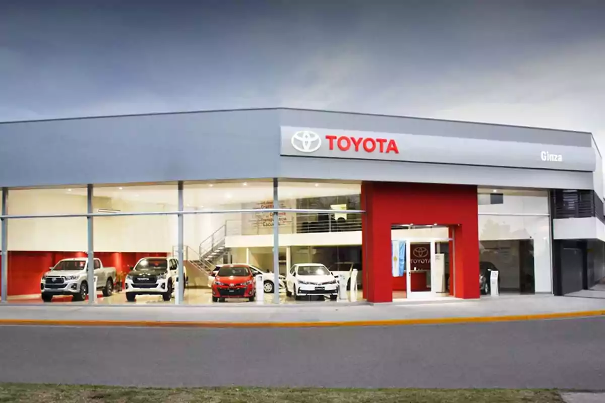 Facade of a Toyota dealership with several cars displayed inside and a large brand sign at the top of the building Facade of a Toyota dealership with several cars displayed inside and a large brand sign at the top of the building
