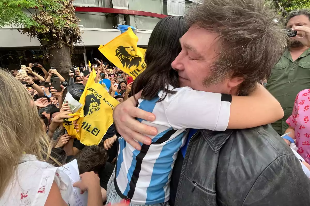Un hombre abraza a una niña con camiseta de Argentina mientras una multitud sostiene banderas amarillas y toma fotos