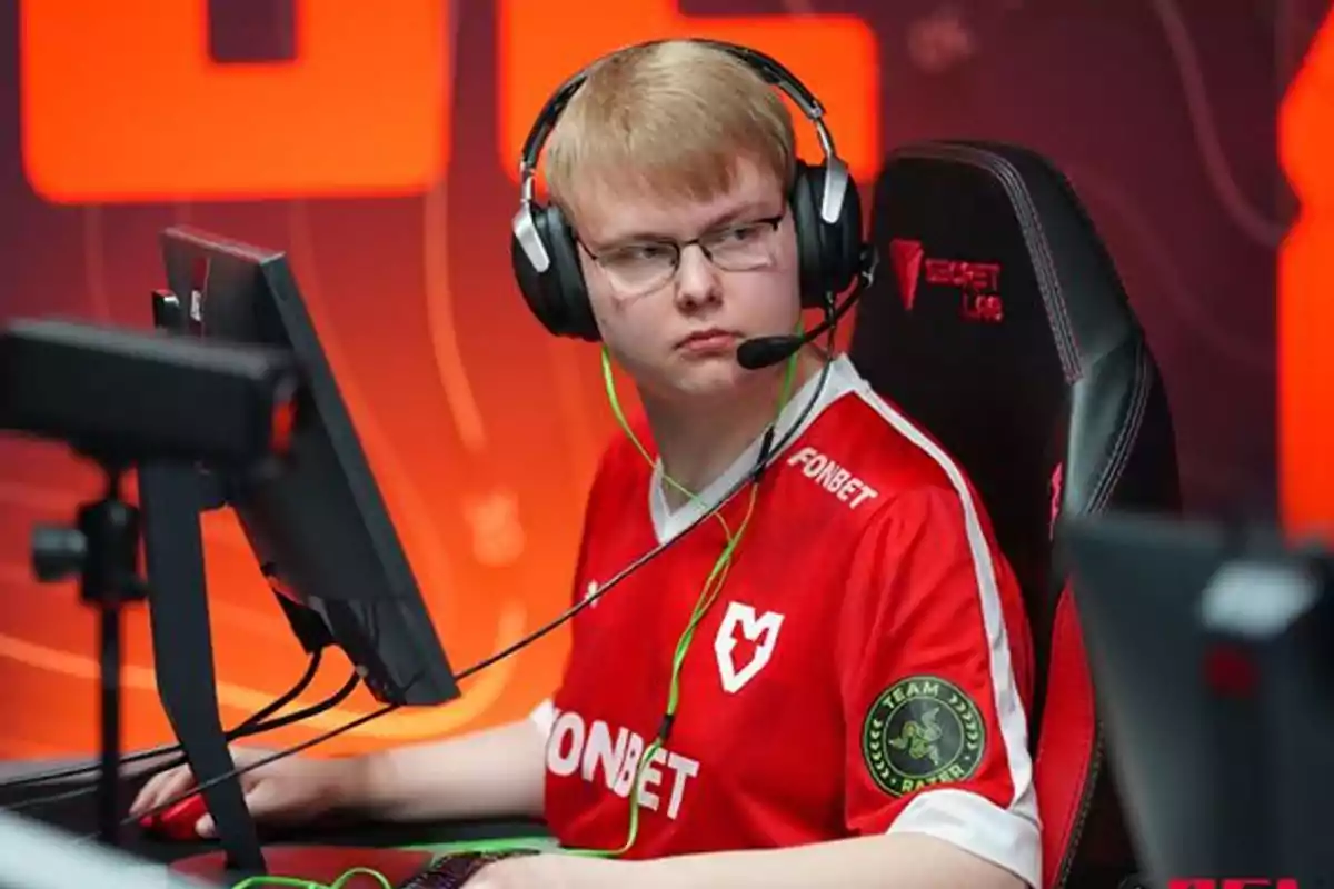 Joven con auriculares y camiseta roja de equipo de esports sentado frente a una computadora en una competencia de videojuegos Joven con auriculares y camiseta roja de equipo de esports sentado frente a una computadora en una competencia de videojuegos