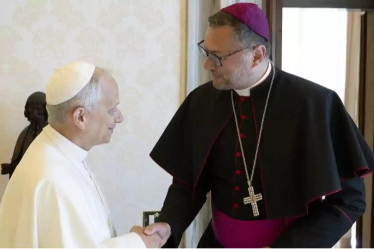 Dos religiosos católicos se saludan cordialmente dándose la mano dentro de una habitación elegantemente decorada. Dos religiosos católicos se saludan cordialmente dándose la mano dentro de una habitación elegantemente decorada.