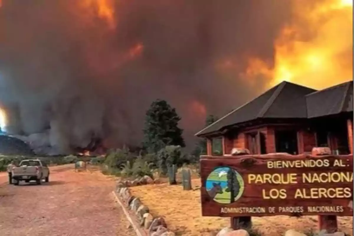 Incendio forestal de gran magnitud en el Parque Nacional Los Alerces con una gran nube de humo y fuego al fondo y un cartel de bienvenida en primer plano Incendio forestal de gran magnitud en el Parque Nacional Los Alerces con una gran nube de humo y fuego al fondo y un cartel de bienvenida en primer plano