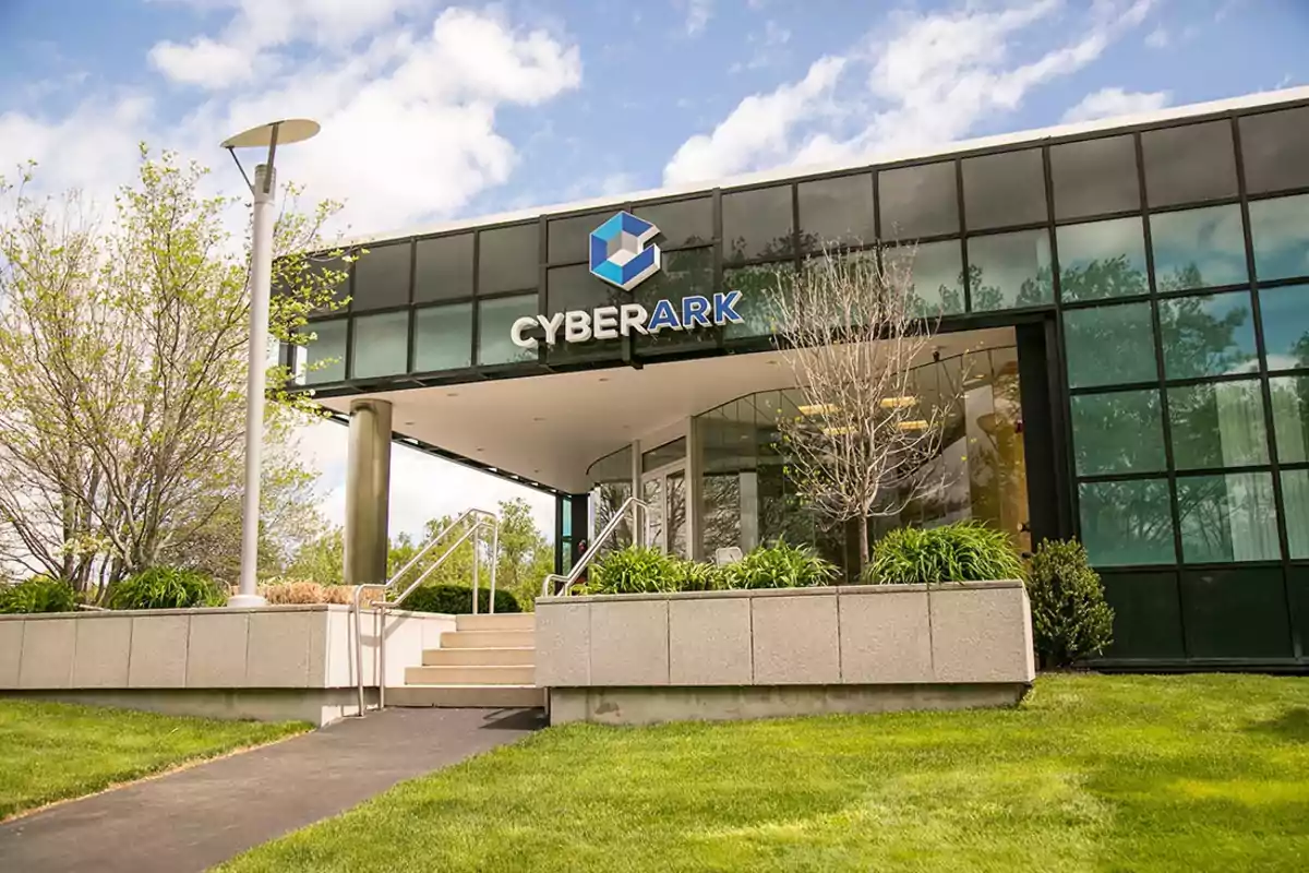 Facade of a modern building with the CyberArk logo, surrounded by grass and trees under a partly cloudy sky