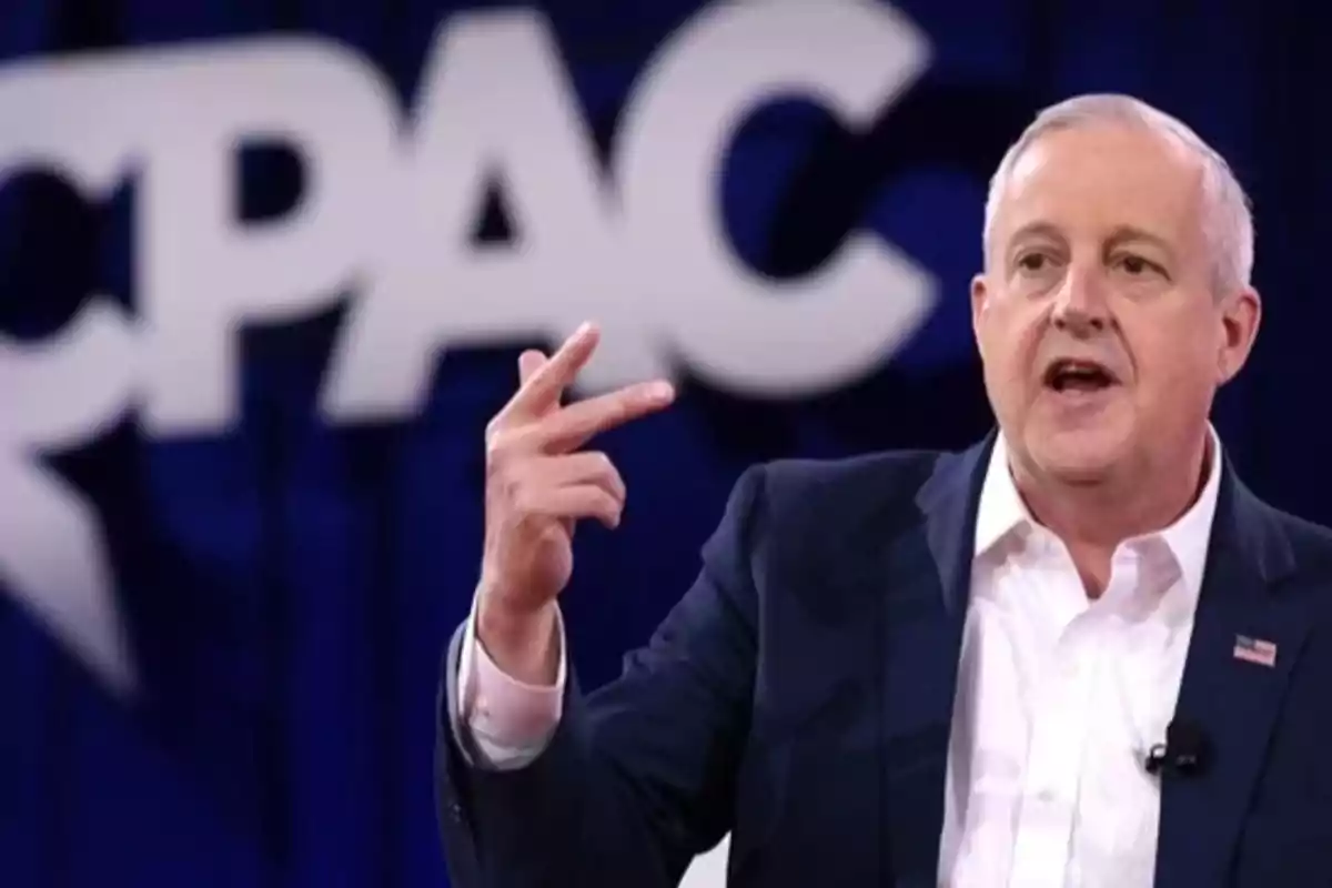 Hombre de cabello canoso con traje oscuro y camisa blanca hablando en un escenario con el logo de CPAC de fondo Hombre de cabello canoso con traje oscuro y camisa blanca hablando en un escenario con el logo de CPAC de fondo