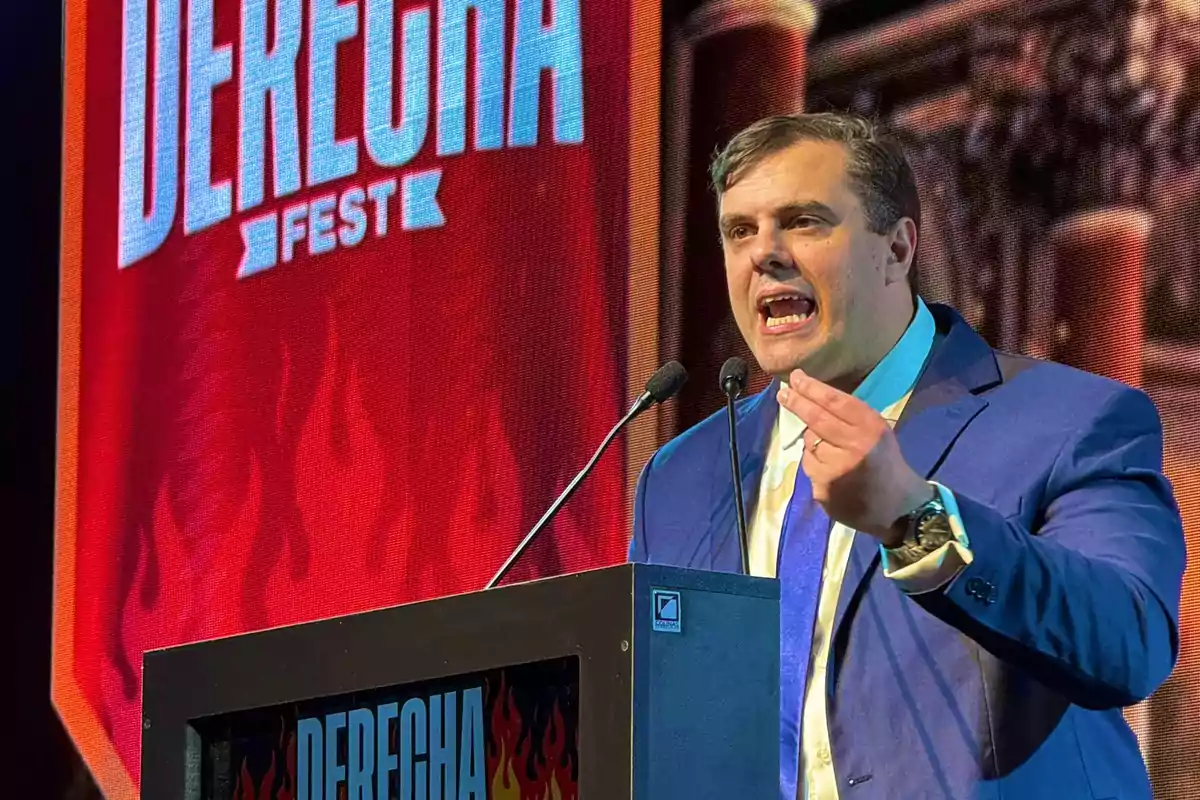 Hombre con traje azul hablando apasionadamente en un podio con el letrero DERECHA FEST al fondo