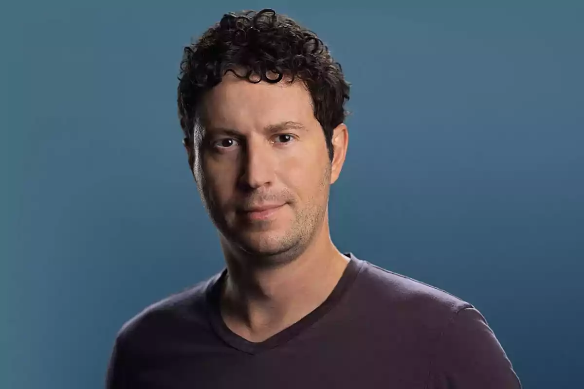 Curly-haired man with short hair wearing a dark t-jersey posing in front of a blue background Curly-haired man with short hair wearing a dark t-jersey posing in front of a blue background