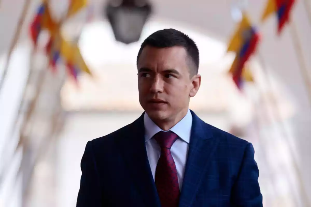 Short-haired man in a blue suit and red tie in a formal setting with blurred flags in the background Short-haired man in a blue suit and red tie in a formal setting with blurred flags in the background