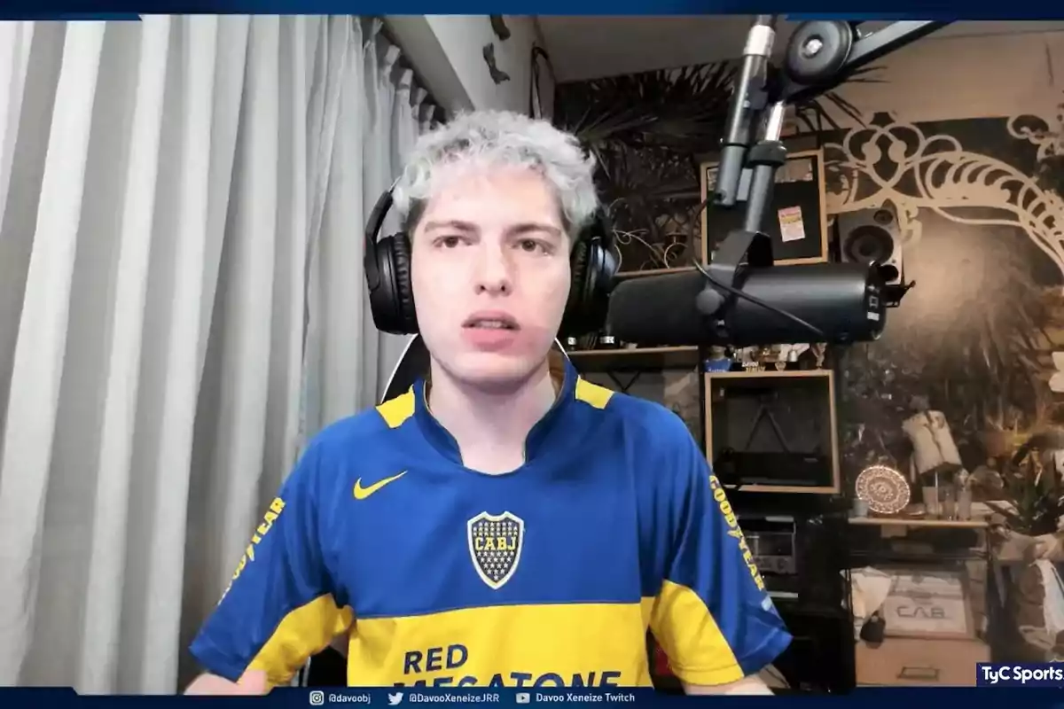 Persona con cabello corto y teñido de rubio usando auriculares y camiseta de Boca Juniors frente a un micrófono en una habitación decorada con estanterías y cortinas claras Persona con cabello corto y teñido de rubio usando auriculares y camiseta de Boca Juniors frente a un micrófono en una habitación decorada con estanterías y cortinas claras