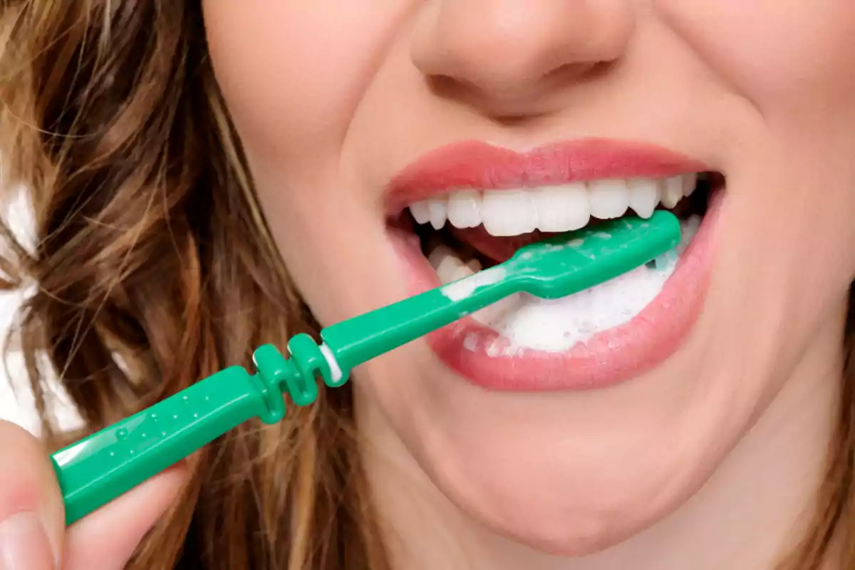 Mujer cepillándose los dientes con un cepillo verde y pasta dental espumosa Mujer cepillándose los dientes con un cepillo verde y pasta dental espumosa