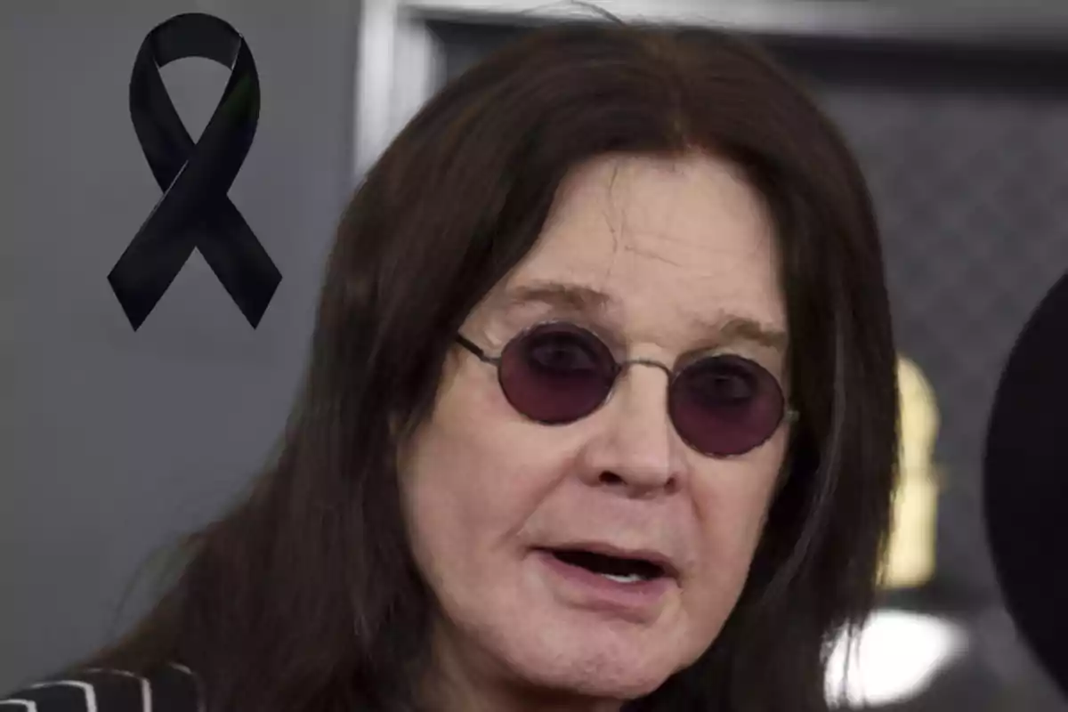 Hombre de cabello largo y gafas oscuras con un moño negro de luto en la esquina superior izquierda