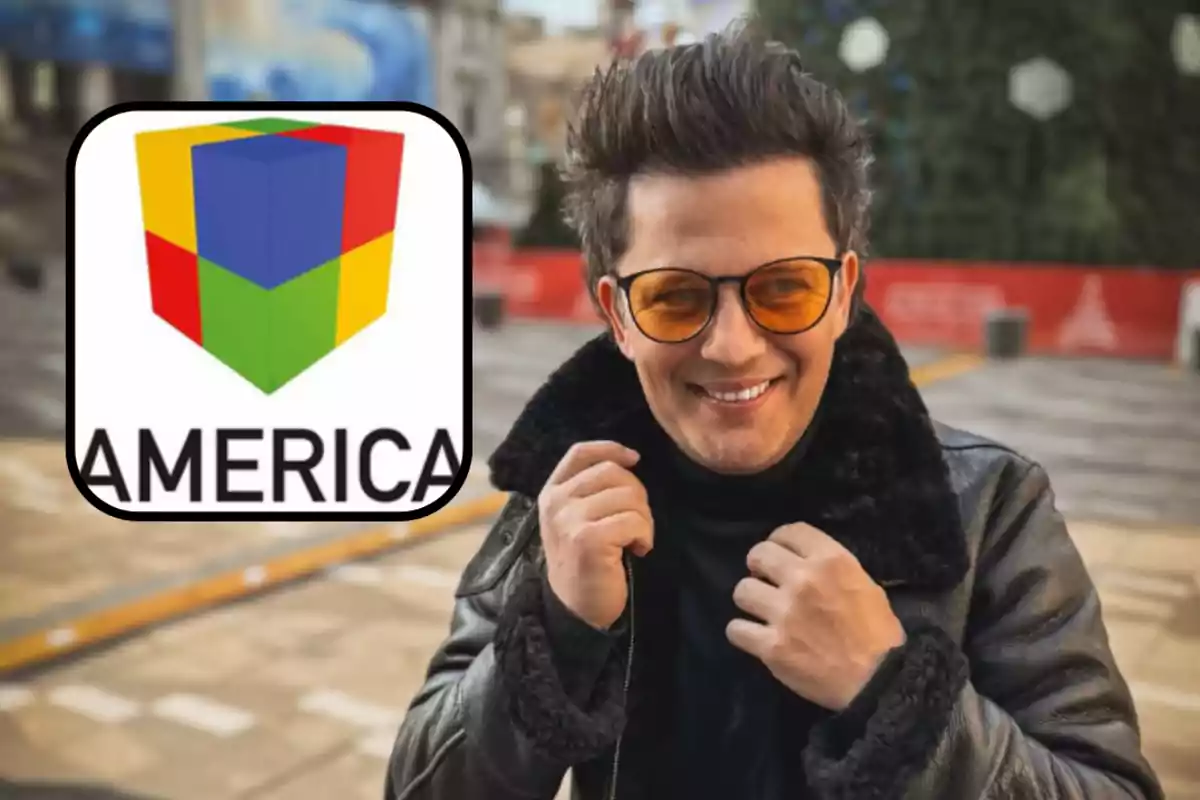 Hombre con gafas de sol naranjas y chaqueta de cuero sonríe al aire libre junto al logo de un canal de televisión que dice America