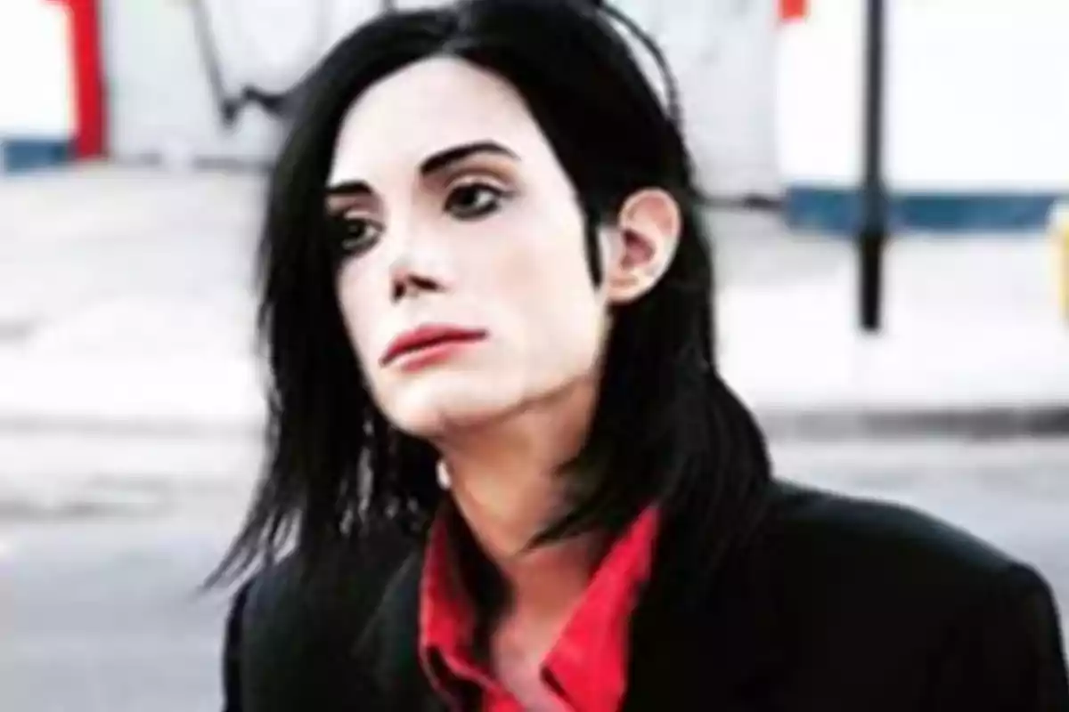 Persona con cabello largo y oscuro, piel clara y labios pintados, usando camisa roja y saco negro en un entorno urbano desenfocado.