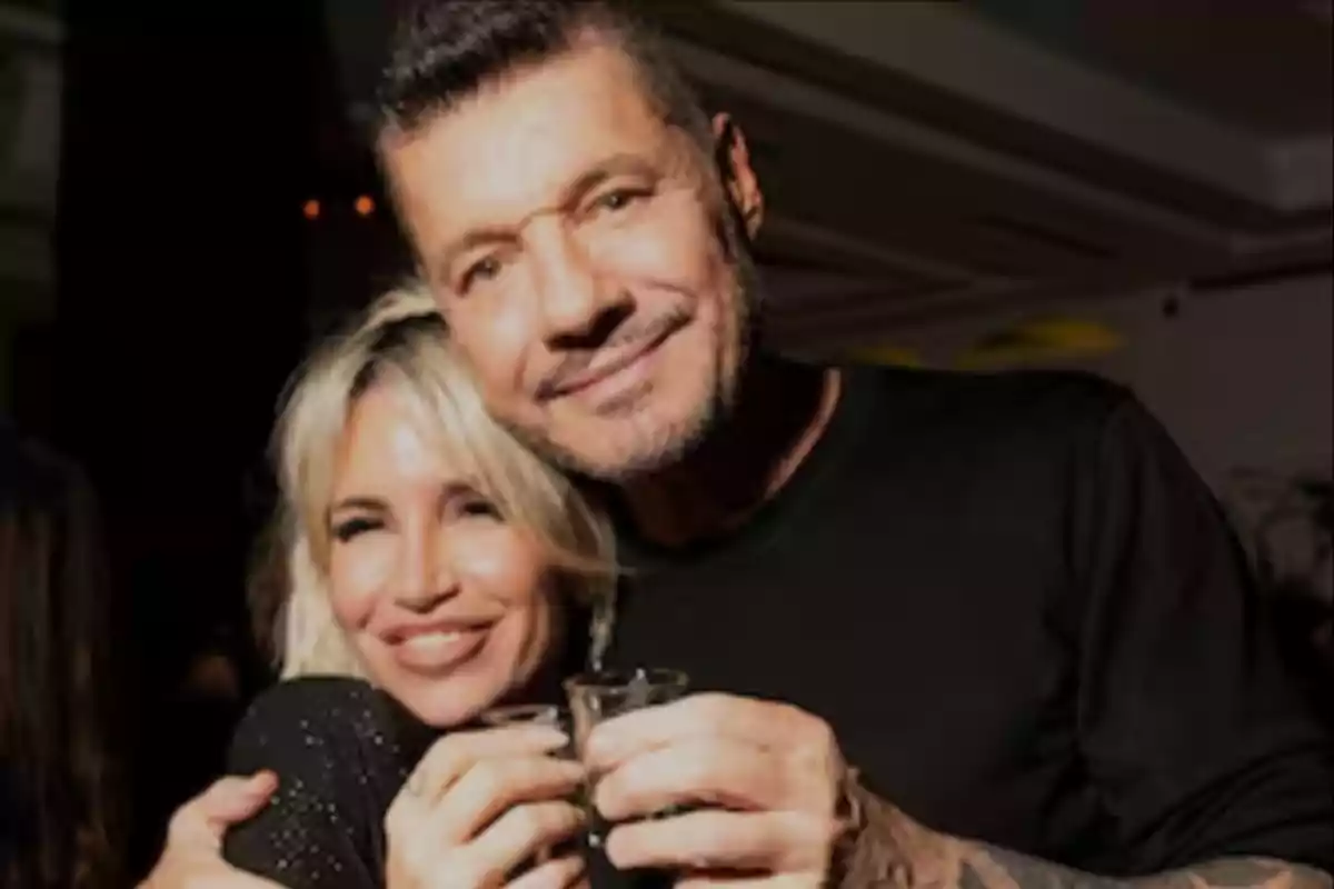 A couple smiles, hugging each other while holding small glasses at a party. A couple smiles, hugging each other while holding small glasses at a party.