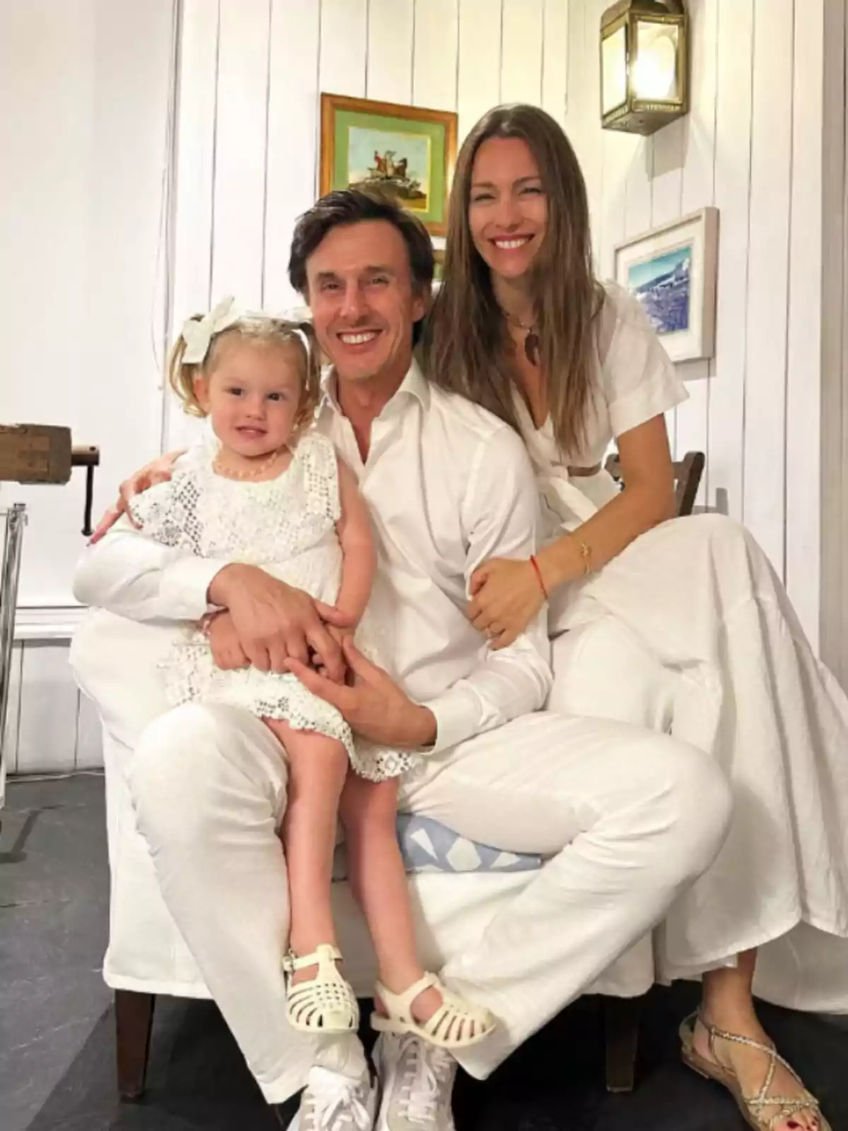 Smiling family dressed in white posing together in a room decorated with paintings and white wooden walls Smiling family dressed in white posing together in a room decorated with paintings and white wooden walls