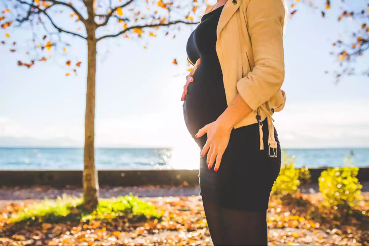 Pregnant woman standing outdoors by a lake on a sunny autumn day