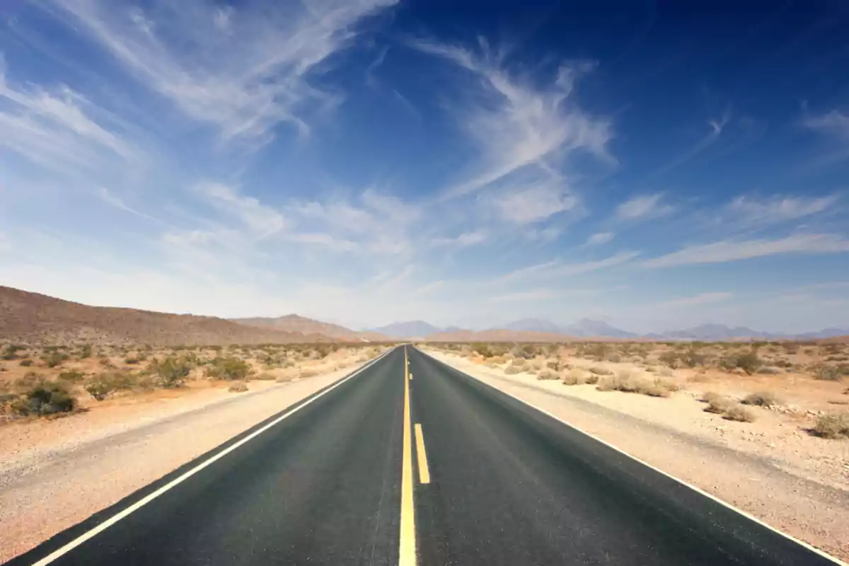 Paved road crossing a desert under a blue sky with scattered clouds