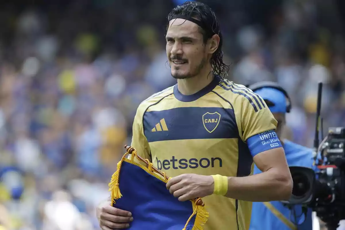Futbolista con camiseta amarilla y azul de Boca Juniors sosteniendo un banderín en el campo de juego