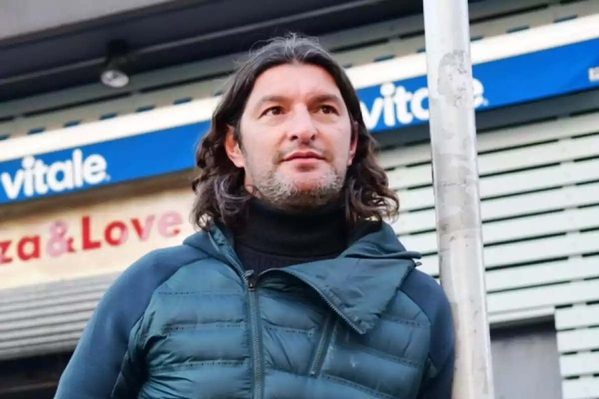 Hombre de cabello largo y barba corta con chaqueta azul parado frente a un letrero azul y blanco en la calle Hombre de cabello largo y barba corta con chaqueta azul parado frente a un letrero azul y blanco en la calle
