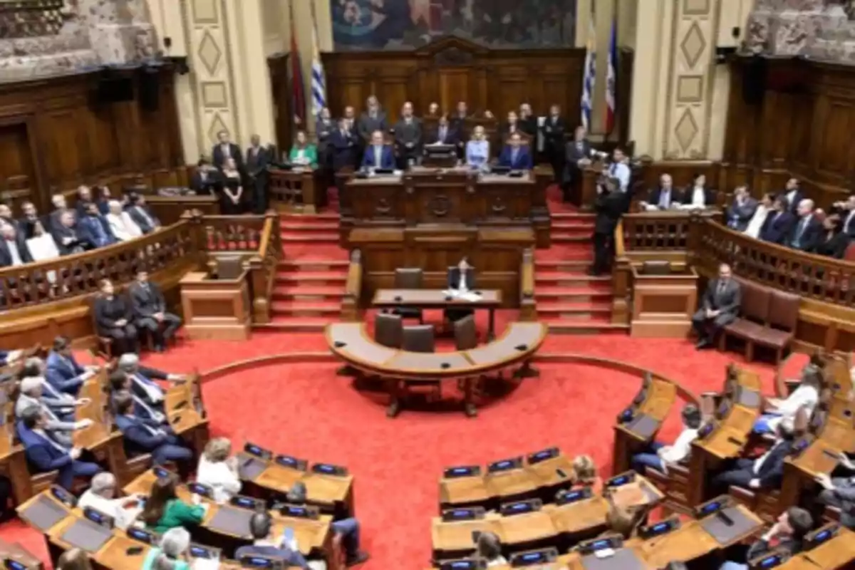 Overview of the interior of a parliament with several people seated on benches and others standing in the upper area in front of a main platform Overview of the interior of a parliament with several people seated on benches and others standing in the upper area in front of a main platform