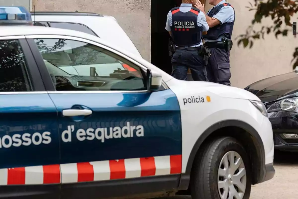 Patrulla de los Mossos d'Esquadra con dos agentes conversando junto a un edificio