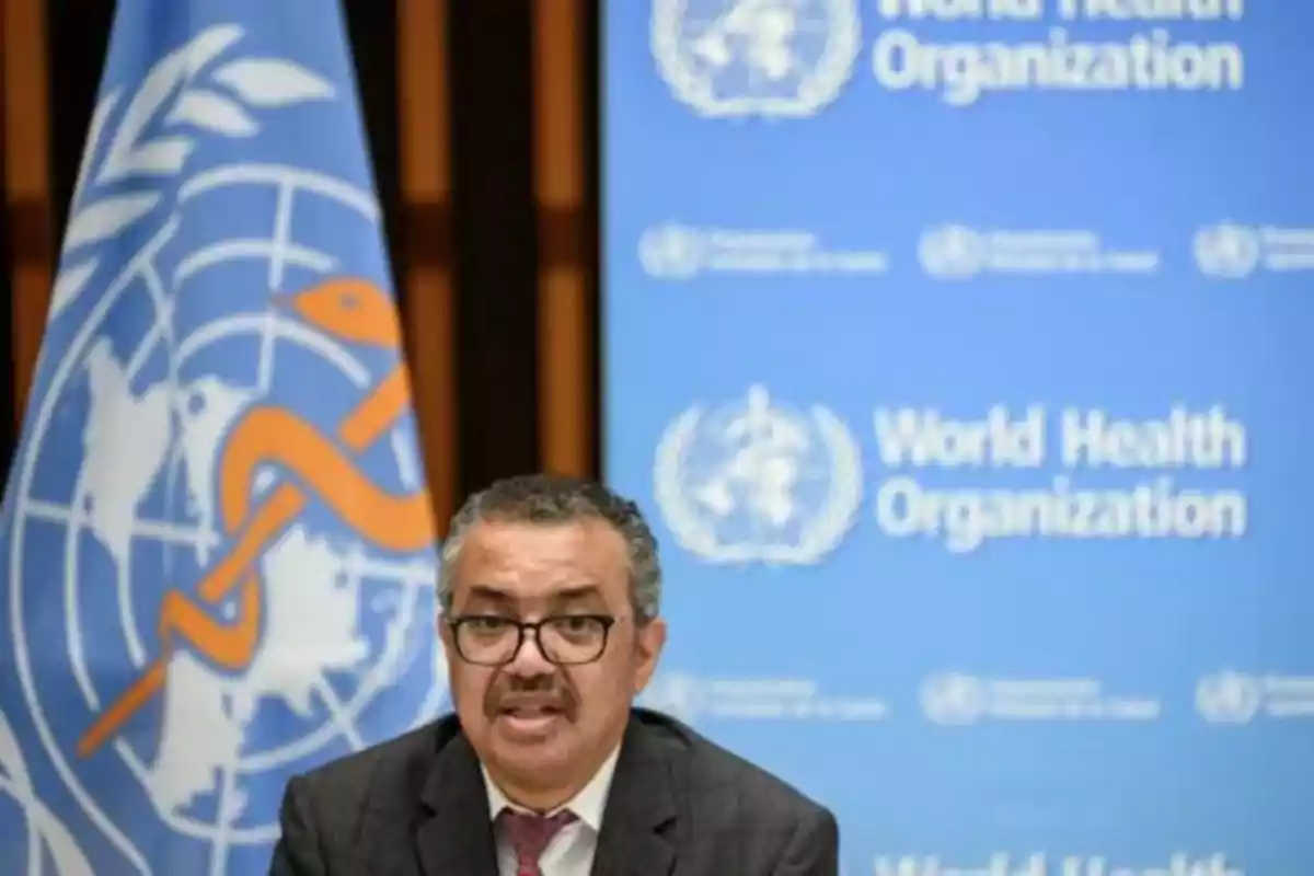 Hombre con gafas y bigote hablando frente a un fondo azul con el logotipo y nombre de la Organización Mundial de la Salud Hombre con gafas y bigote hablando frente a un fondo azul con el logotipo y nombre de la Organización Mundial de la Salud