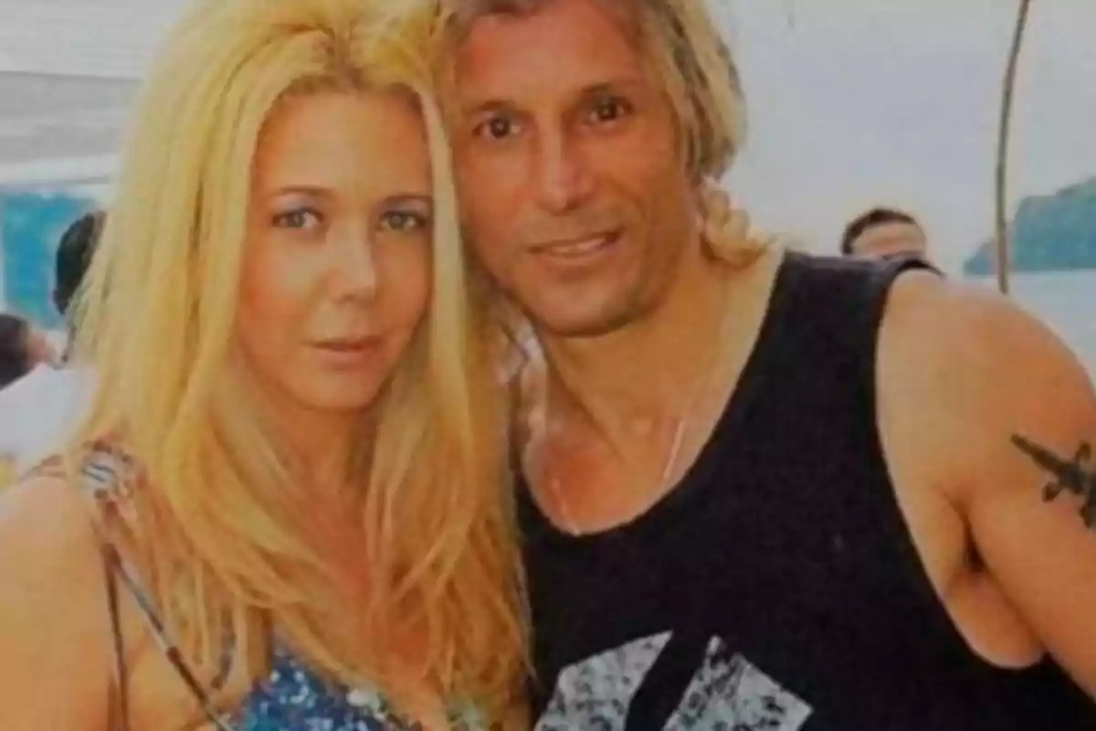 A blonde-haired couple poses together outdoors, both looking at the camera and appearing to be in a summer setting. A blonde-haired couple poses together outdoors, both looking at the camera and appearing to be in a summer setting.