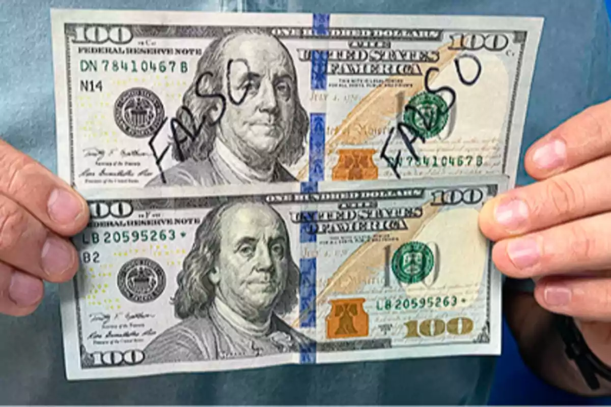 Persona sosteniendo dos billetes de cien dólares estadounidenses, uno de ellos con la palabra falso escrita en grande