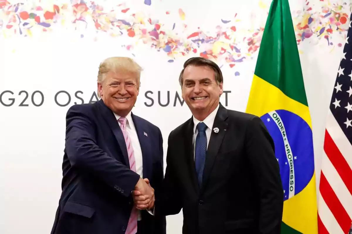 Two men in suits shake hands and smile in front of the flags of Brazil and the United States at an international summit. Two men in suits shake hands and smile in front of the flags of Brazil and the United States at an international summit.