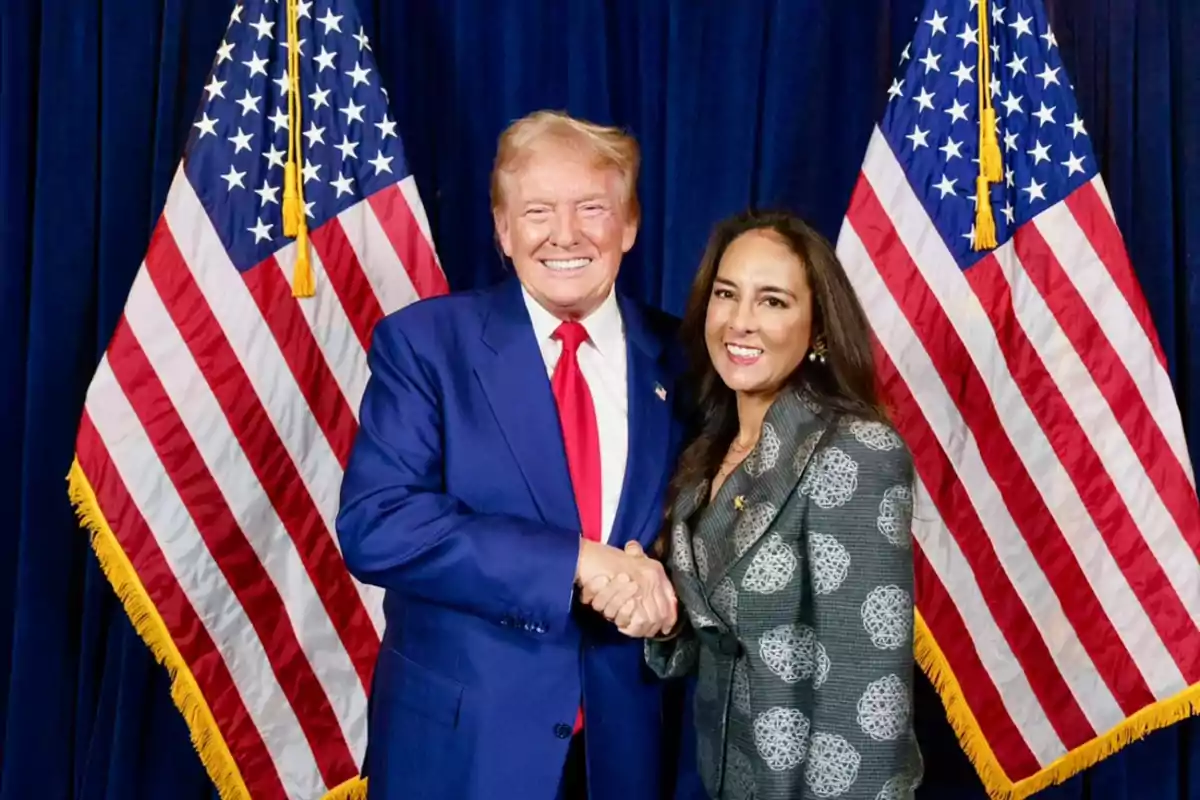 Dos personas sonríen y se dan la mano frente a dos banderas de Estados Unidos Dos personas sonríen y se dan la mano frente a dos banderas de Estados Unidos