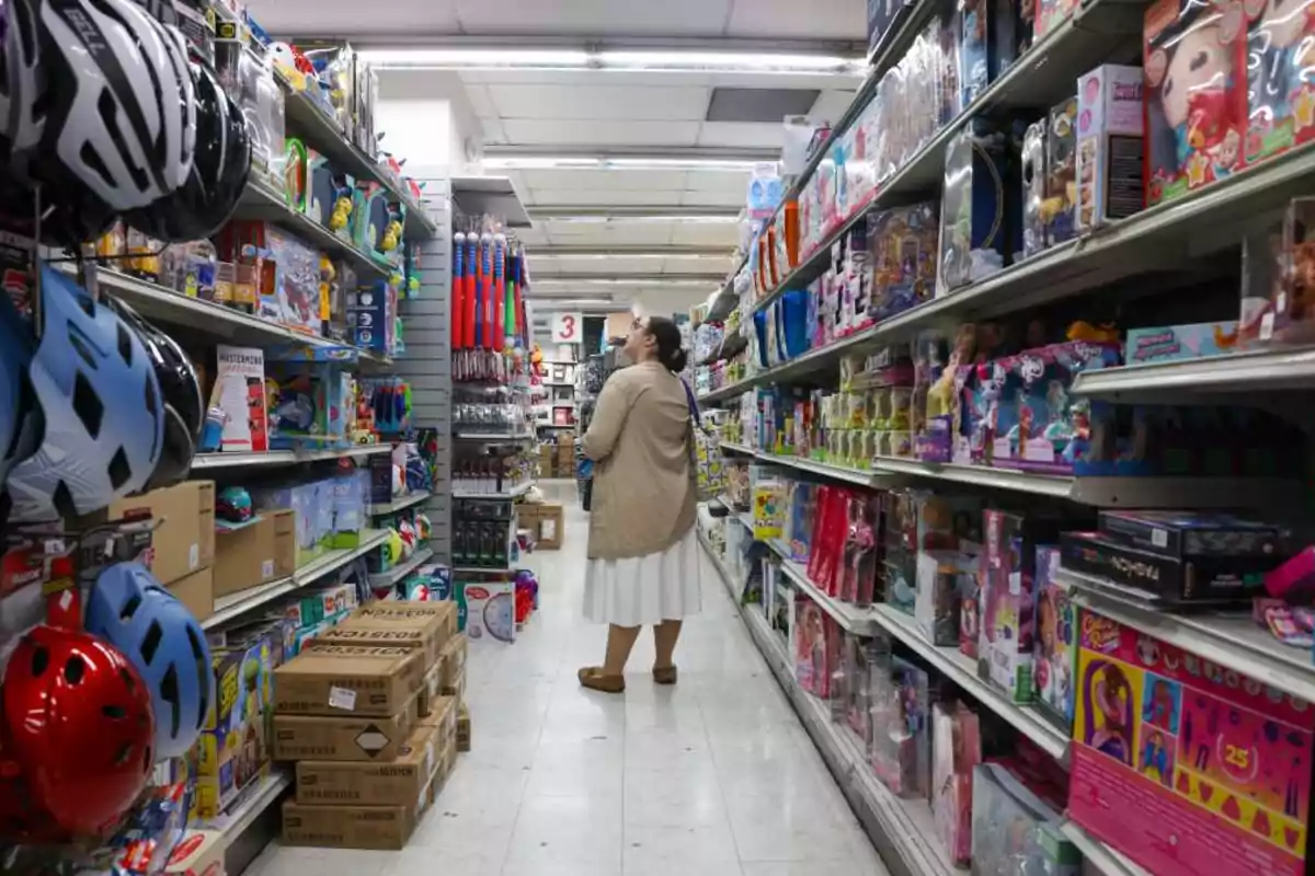 Mujer de pie en el pasillo de una tienda rodeada de estantes llenos de juguetes y cascos de bicicleta Mujer de pie en el pasillo de una tienda rodeada de estantes llenos de juguetes y cascos de bicicleta