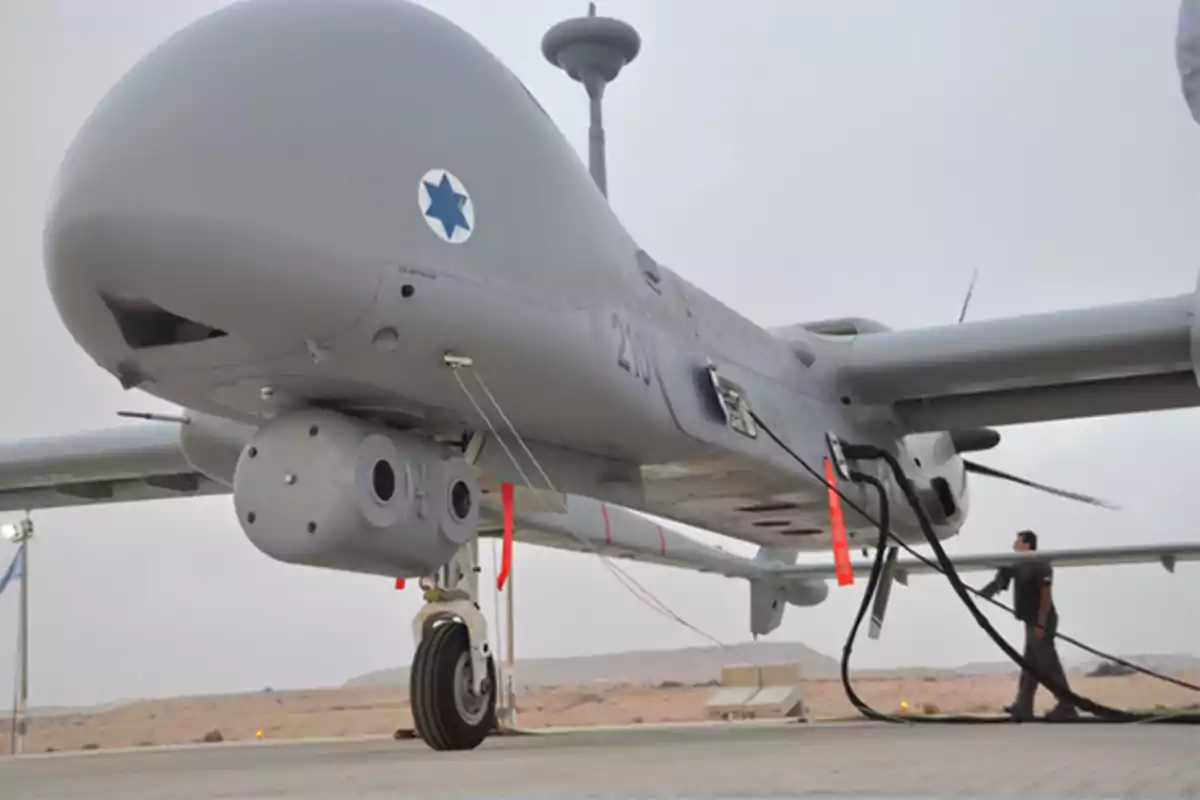 Dron militar gris en tierra siendo revisado por una persona en una base aérea en el desierto Dron militar gris en tierra siendo revisado por una persona en una base aérea en el desierto