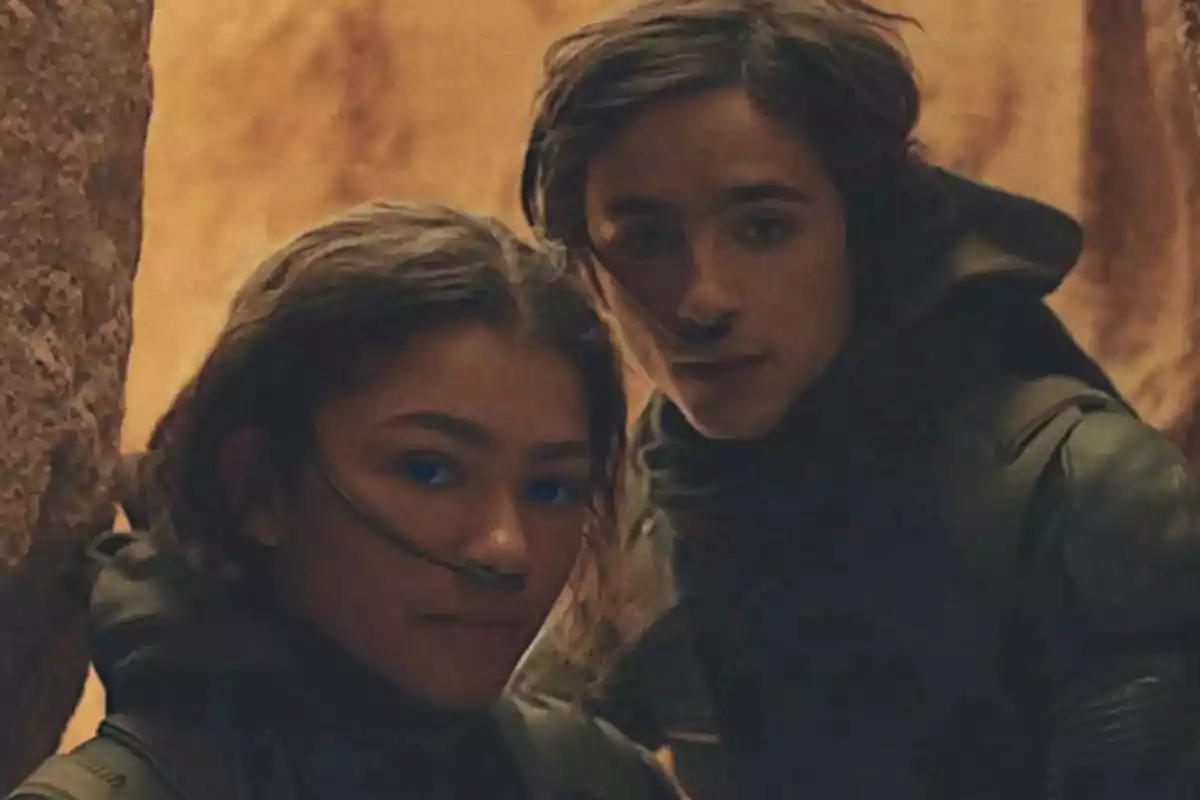 Two people in dark suits with tubes in their noses are in a rocky, arid environment; one of them has bright blue eyes. Two people in dark suits with tubes in their noses are in a rocky, arid environment; one of them has bright blue eyes.