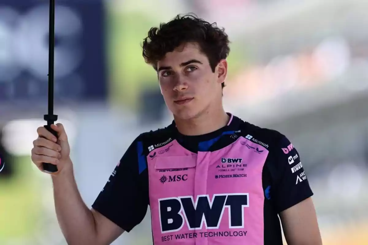 Young man in a BWT Alpine motorsport team uniform holding an umbrella in an outdoor setting Young man in a BWT Alpine motorsport team uniform holding an umbrella in an outdoor setting