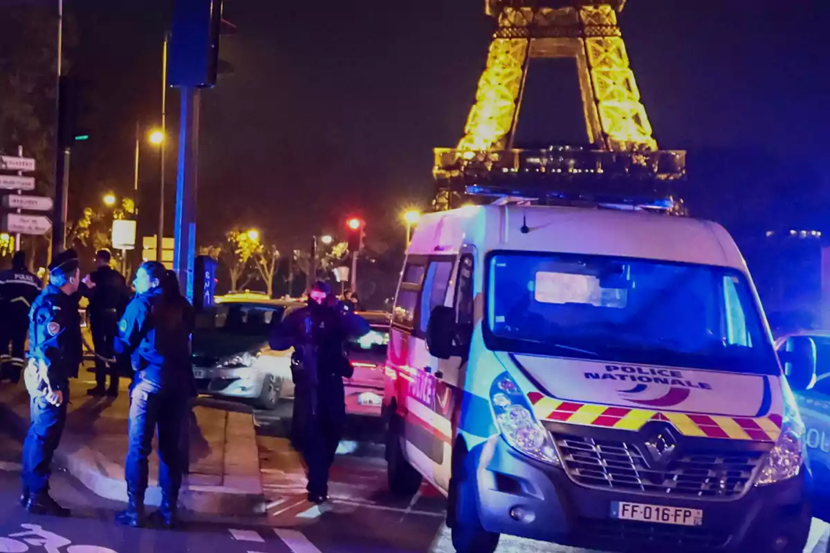 Policías y una patrulla de la policía nacional de Francia están en una calle de París por la noche con la Torre Eiffel iluminada al fondo