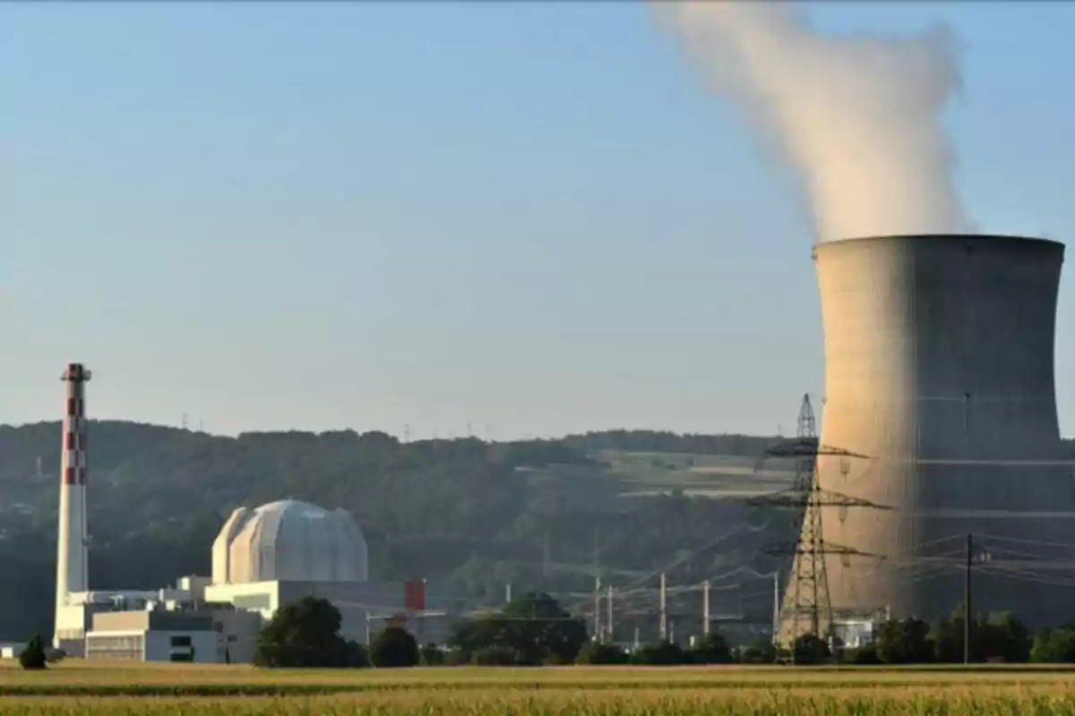 Central nuclear con torre de enfriamiento emitiendo vapor en un entorno rural con colinas al fondo