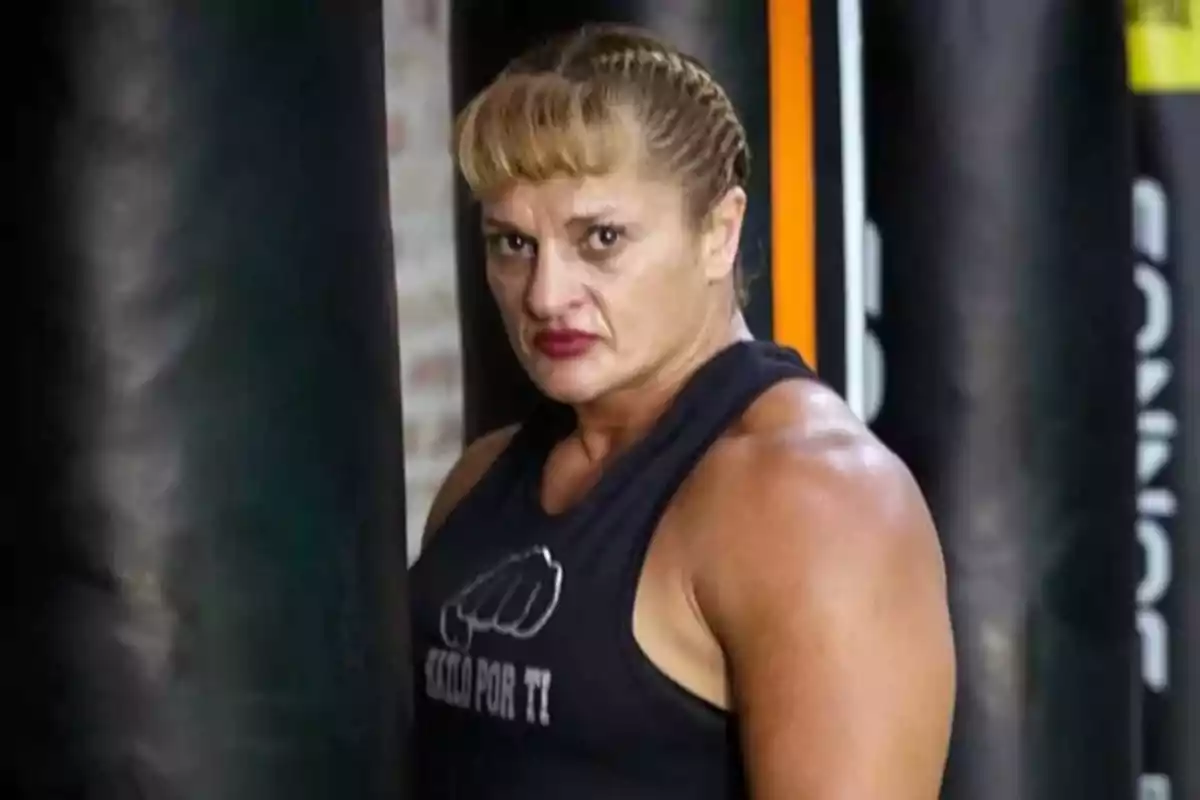Mujer musculosa con camiseta sin mangas negra y trenza, de pie junto a un costal de boxeo en un gimnasio Mujer musculosa con camiseta sin mangas negra y trenza, de pie junto a un costal de boxeo en un gimnasio