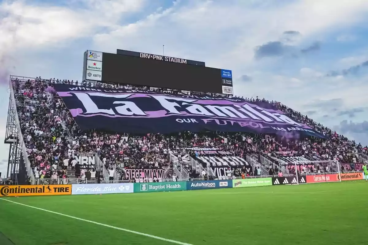 Aficionados en un estadio de fútbol despliegan una gran manta que dice La Familia mientras animan a su equipo con banderas y pancartas